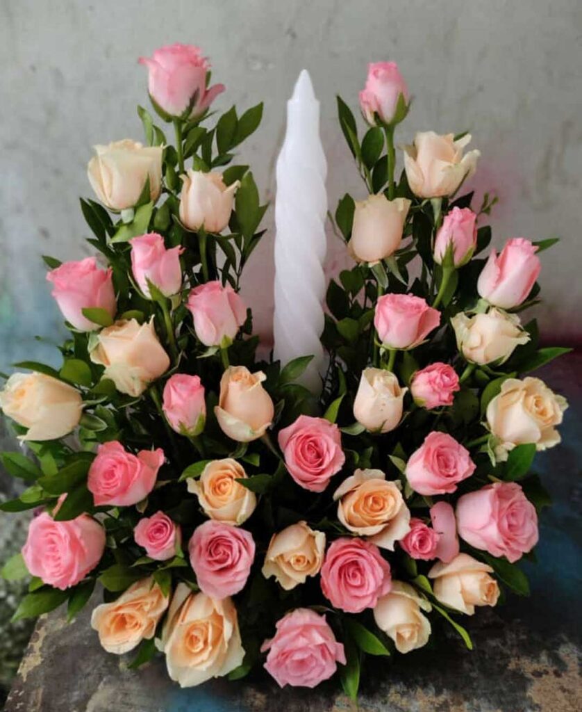 A wreath adorned with peach and pink roses, surrounded by glowing candles. Perfect for expressing condolences and sympathy. Same-day delivery available in Trivandrum.